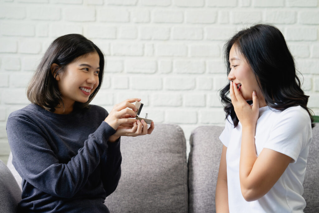 Happy young Asian lesbian couple with wedding rings at home living room. LGBTQ lifestyle concepts.